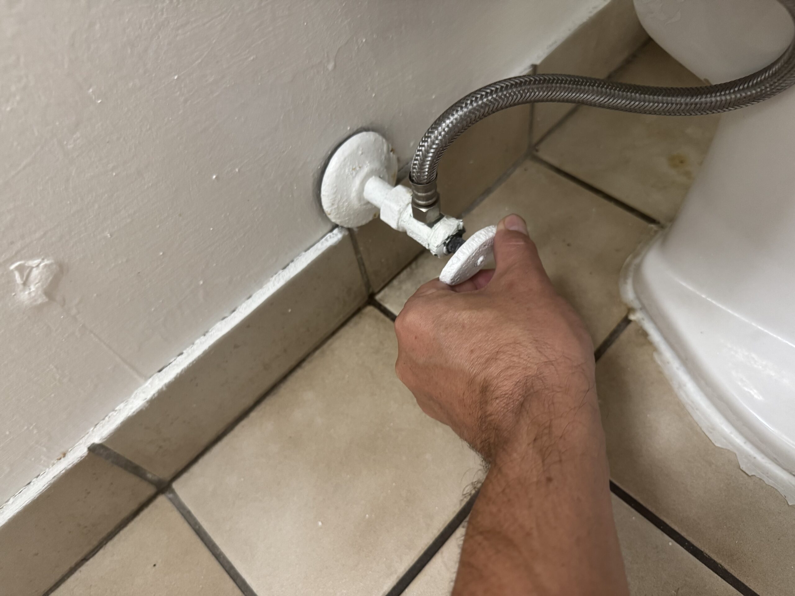 Plumber tightening water supply valve behind toilet for repair or installation.